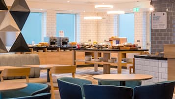 Un espace moderne dédié au petit-déjeuner, avec un buffet, des places assises et un mur recouvert de carreaux propres.