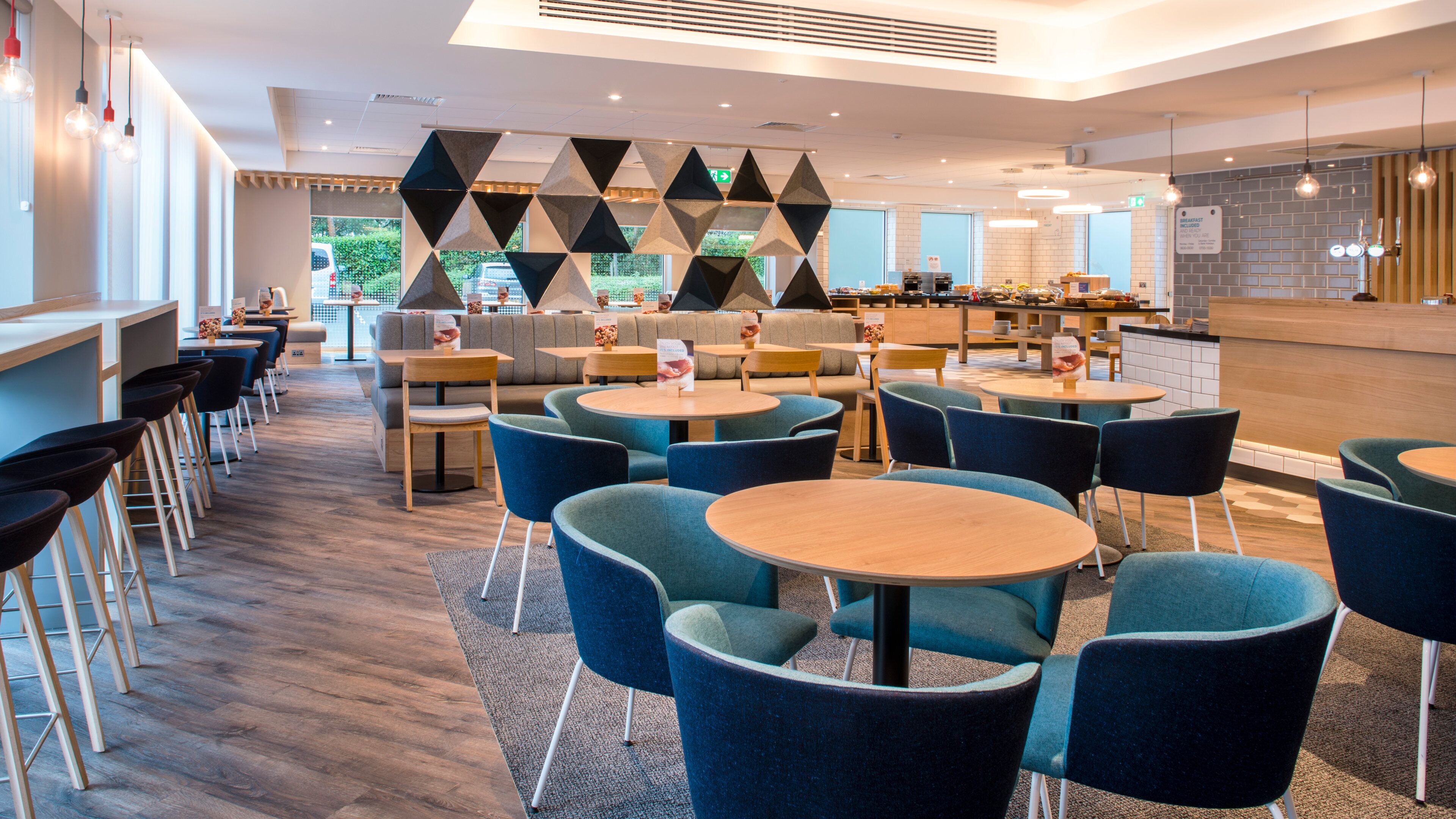 A modern cafe with round tables, blue chairs, and a geometric wall design.