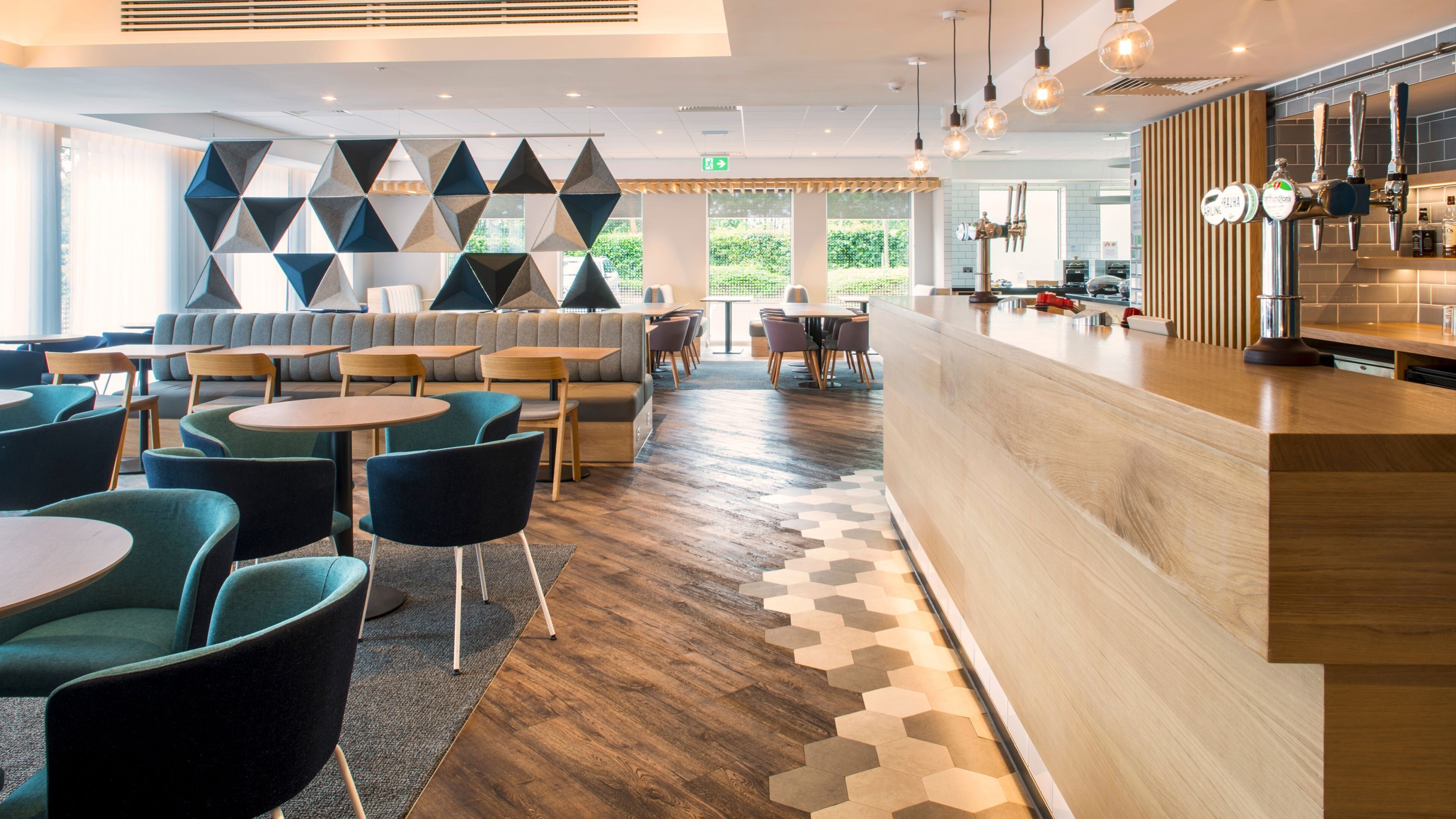 A modern hotel lobby with a bar area, seating arrangements, and a geometric wall design.