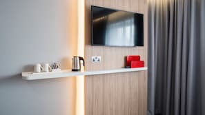 A modern hotel room with a mounted TV, a white shelf with a coffee maker, cups, and condiments, and a red chair. - Holiday Inn Express Oxford-Kassam Stadium by IHG (Oxford)