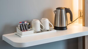 Valkoinen hylly, jonka päällä on kahvinkeitin, kaksi valkoista mukea ja mukiteline, jossa on Nescafe Original -kahvikapseleita.
