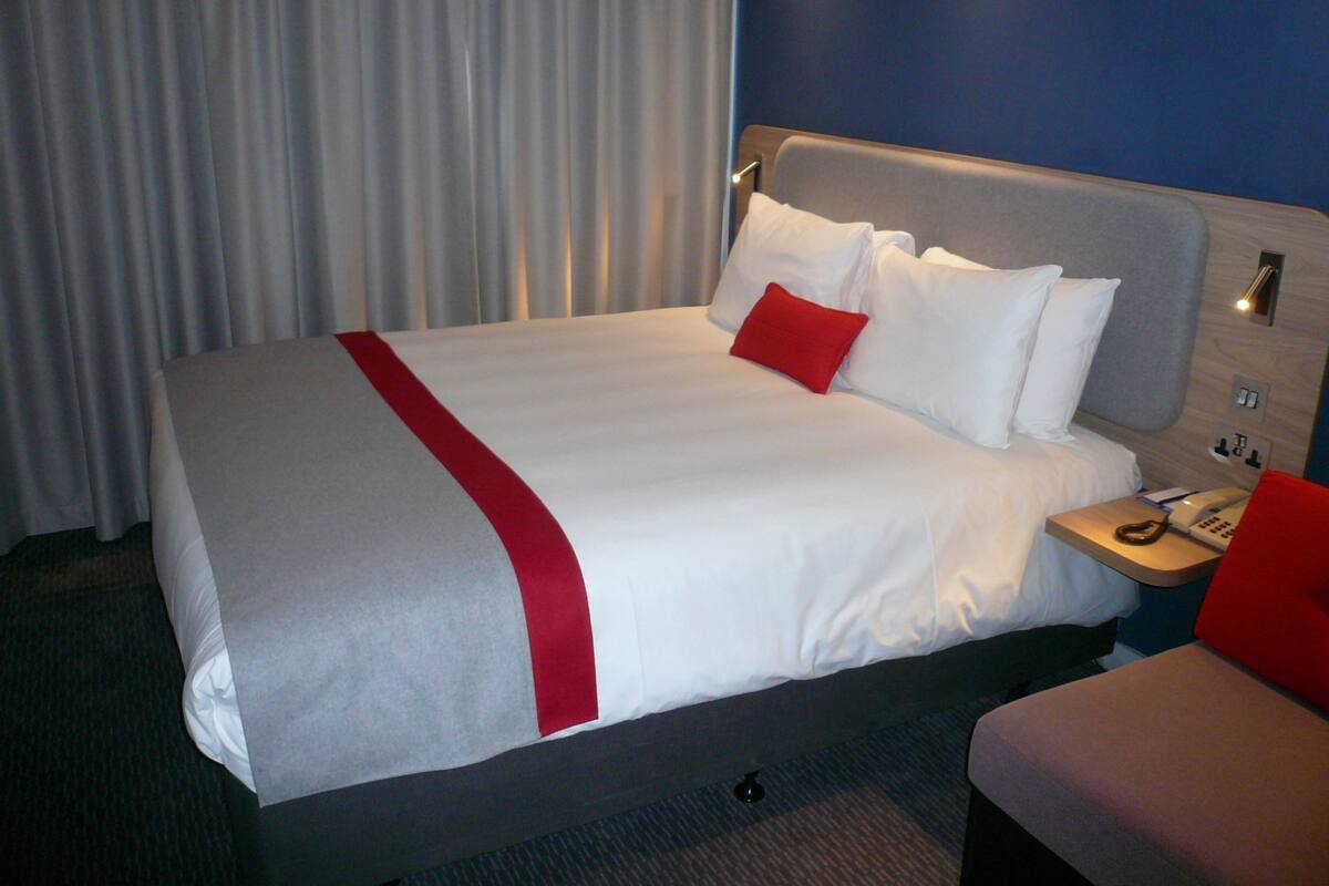 A hotel room with a large bed, a bedside table with a phone, and a red accent pillow.