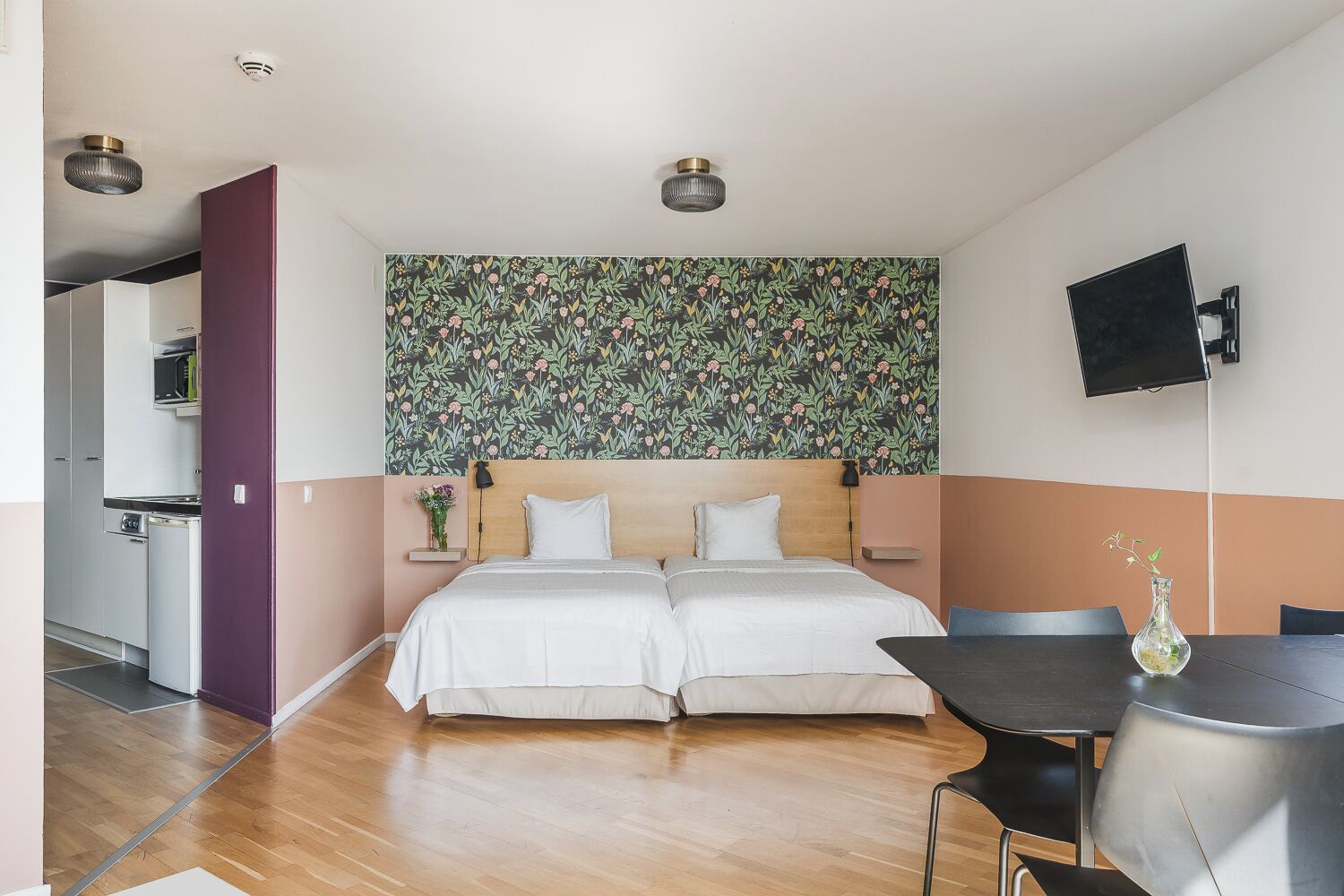 Ein Schlafzimmer mit einem Doppelbett, einem kleinen Tisch mit einer Vase und einem an der Wand befestigten Fernseher.