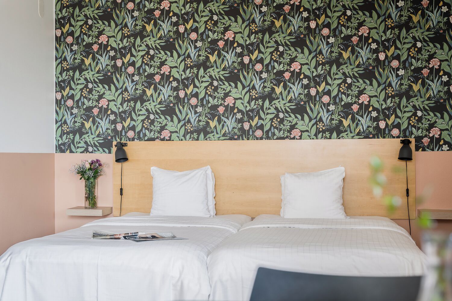 A double bed with white linens, a wooden headboard, and a floral-patterned wallpaper.