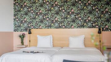 A double bed with white linens, a wooden headboard, and a floral-patterned wallpaper.