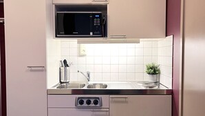 A compact kitchen with white cabinets, a microwave, a sink, and a small countertop with a plant. - 2Home Hotel Apartments (Solna)