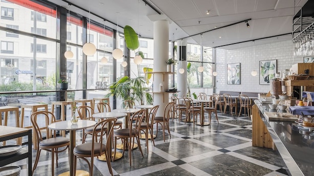 A modern cafe with round tables and chairs, large windows, and a checkered floor. - 2Home Hotel Apartments (Solna)