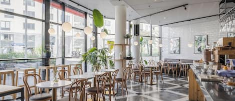 A modern cafe with round tables and chairs, large windows, and a checkered floor.