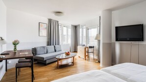 A hotel room with a bed, a sofa, a desk with a lamp, a coffee table, and a TV. - 2Home Hotel Apartments (Solna)
