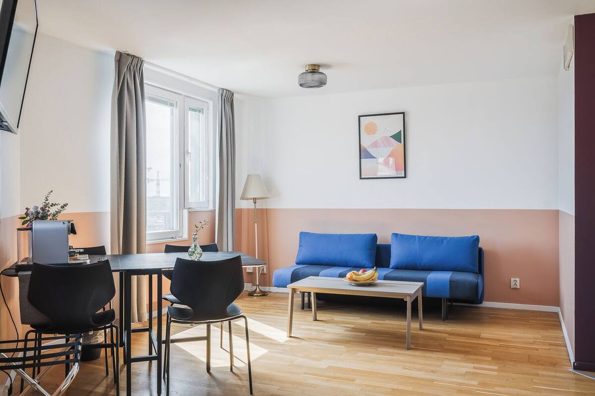 A modern living room with a sofa, a coffee table, a dining table with chairs, a lamp, and a painting on the wall.
