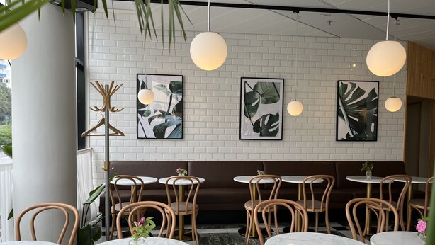 A restaurant interior with round tables and chairs, white brick walls, and abstract art. - 2Home Hotel Apartments (Solna)