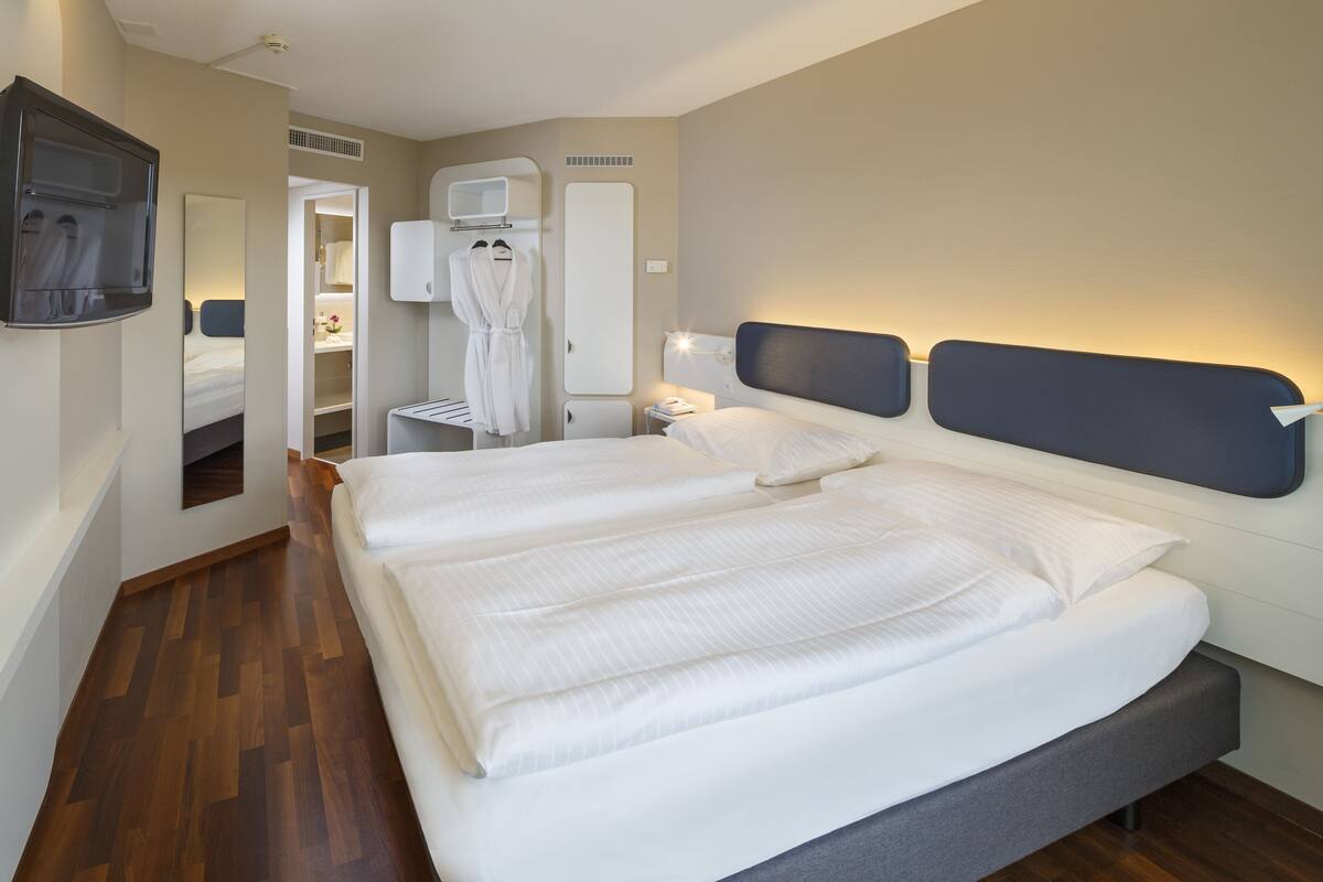 A hotel room with a large bed, a bedside table, a TV, a mirror, and a wardrobe.