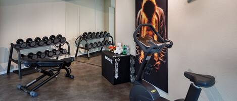 Ein Heim-Fitnessraum mit Kurzhanteln, einer Trainingsbank und einem Ergometer.