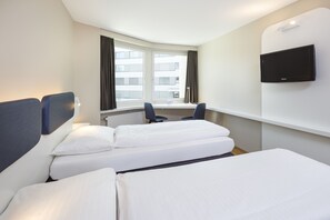 Habitación de hotel con cama, escritorio, silla, televisión y ventana con cortinas.
