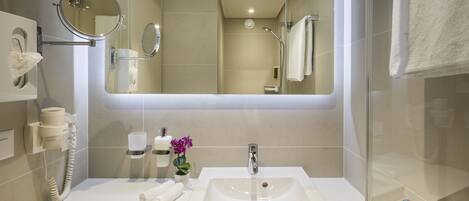 A modern bathroom with a large mirror, a sink, a hairdryer, and a towel rack.