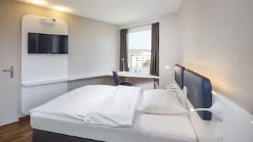 Una habitación de hotel moderna con una cama, un escritorio, una silla, un televisor montado en la pared y una ventana con cortinas.