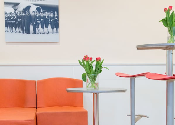 A room with an orange sofa, a small round table with a vase of red tulips, and a chair with a red seat.