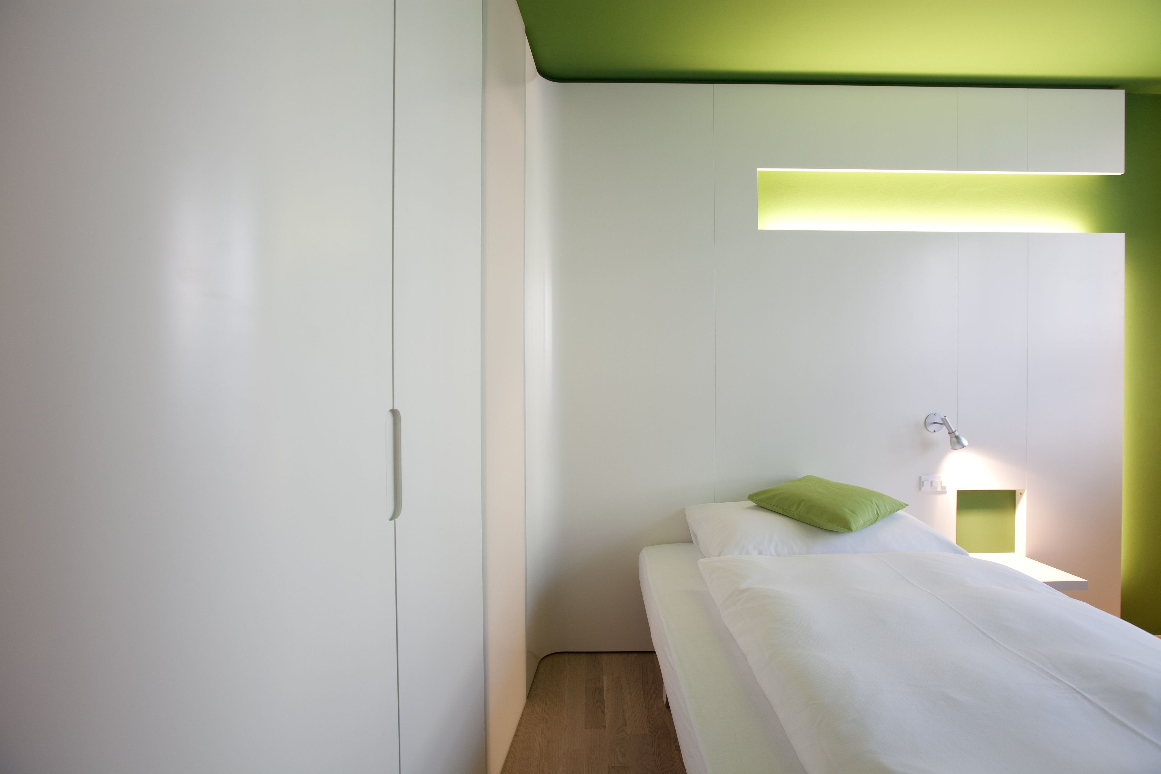 Quarto moderno com cama, mesa de cabeceira e luminária na parede.