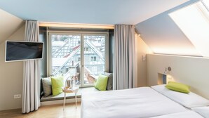 Hotelkamer met een bed, een aan de muur bevestigde televisie, een raam met gordijnen en uitzicht op gebouwen.