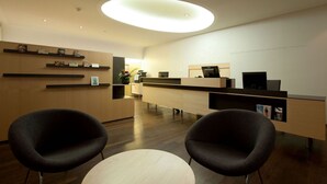 Een moderne receptie met een houten bureau, twee zwarte stoelen, een ronde tafel en een plafondlamp.