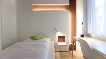 A modern hotel room with a bed, a desk, and a window.