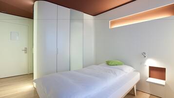Een moderne slaapkamer met een bed, een groen kussen, een inbouwkast en een nachtkastje met lamp.