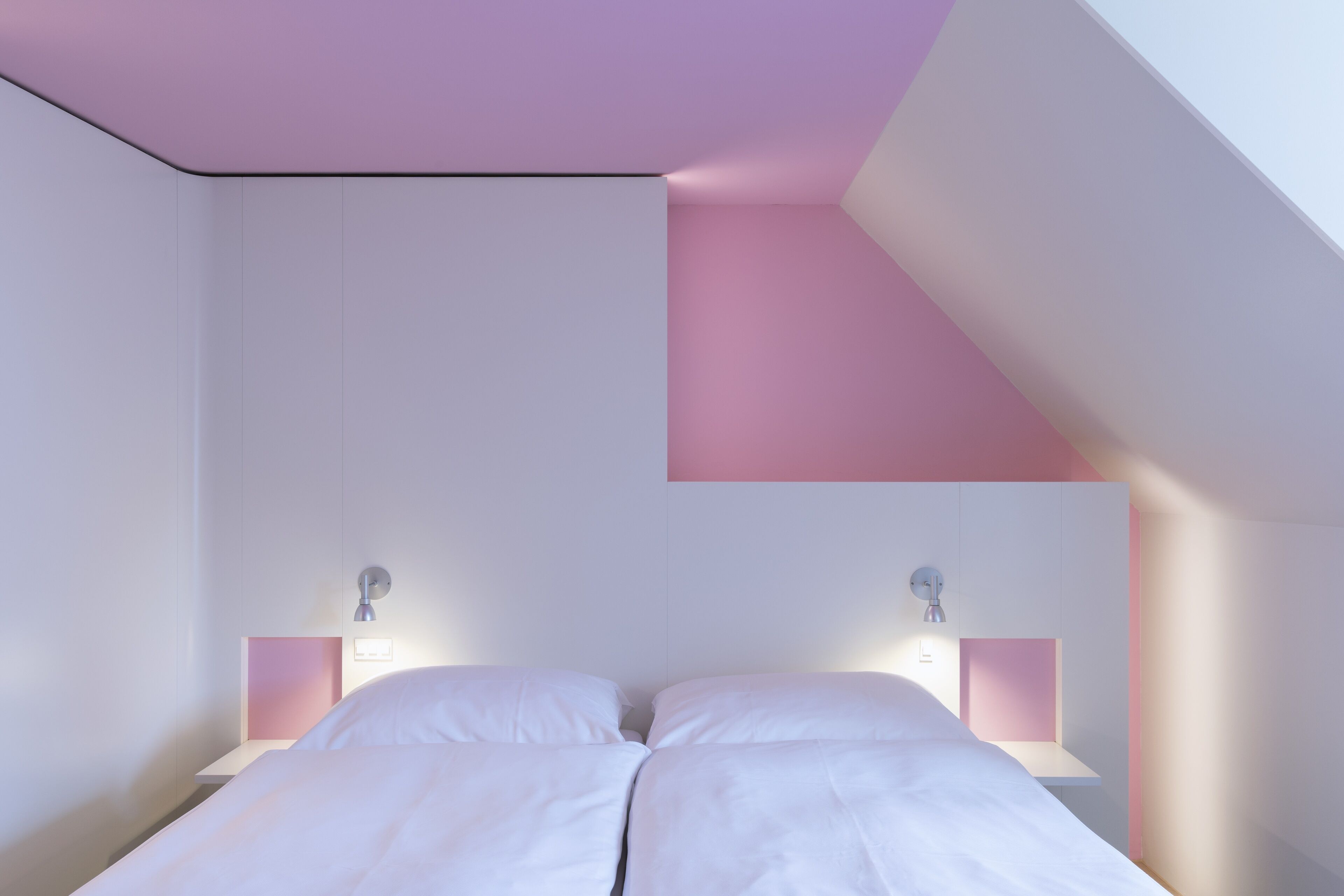 Une chambre à coucher avec un lit placé au centre de la pièce, des murs blancs et un plafond en pente.