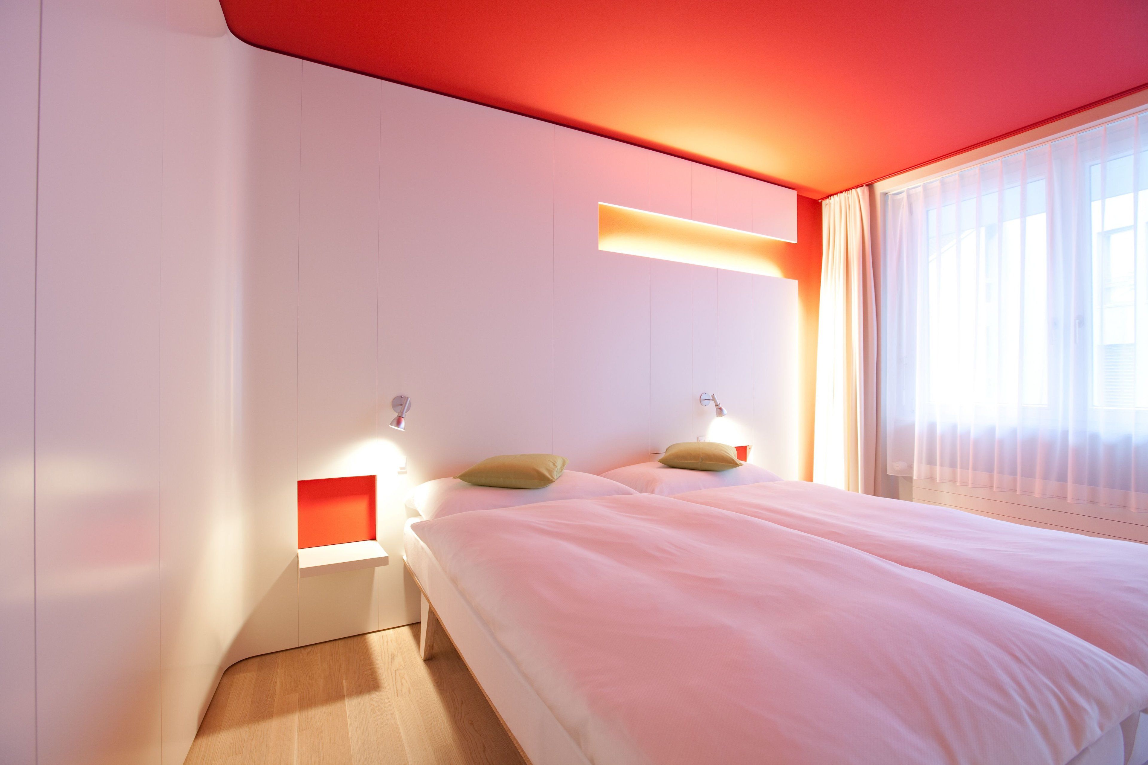 Una habitación de hotel moderna con una cama grande, dos mesitas de noche y un ventanal con cortinas de gasa.