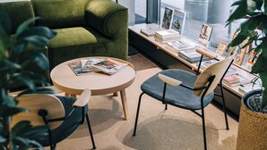 Een gezellig hoekje om te lezen, met een groene bank, een ronde houten tafel en twee stoelen. Achtergrond is een boekenkast met boeken en ingelijste foto's.