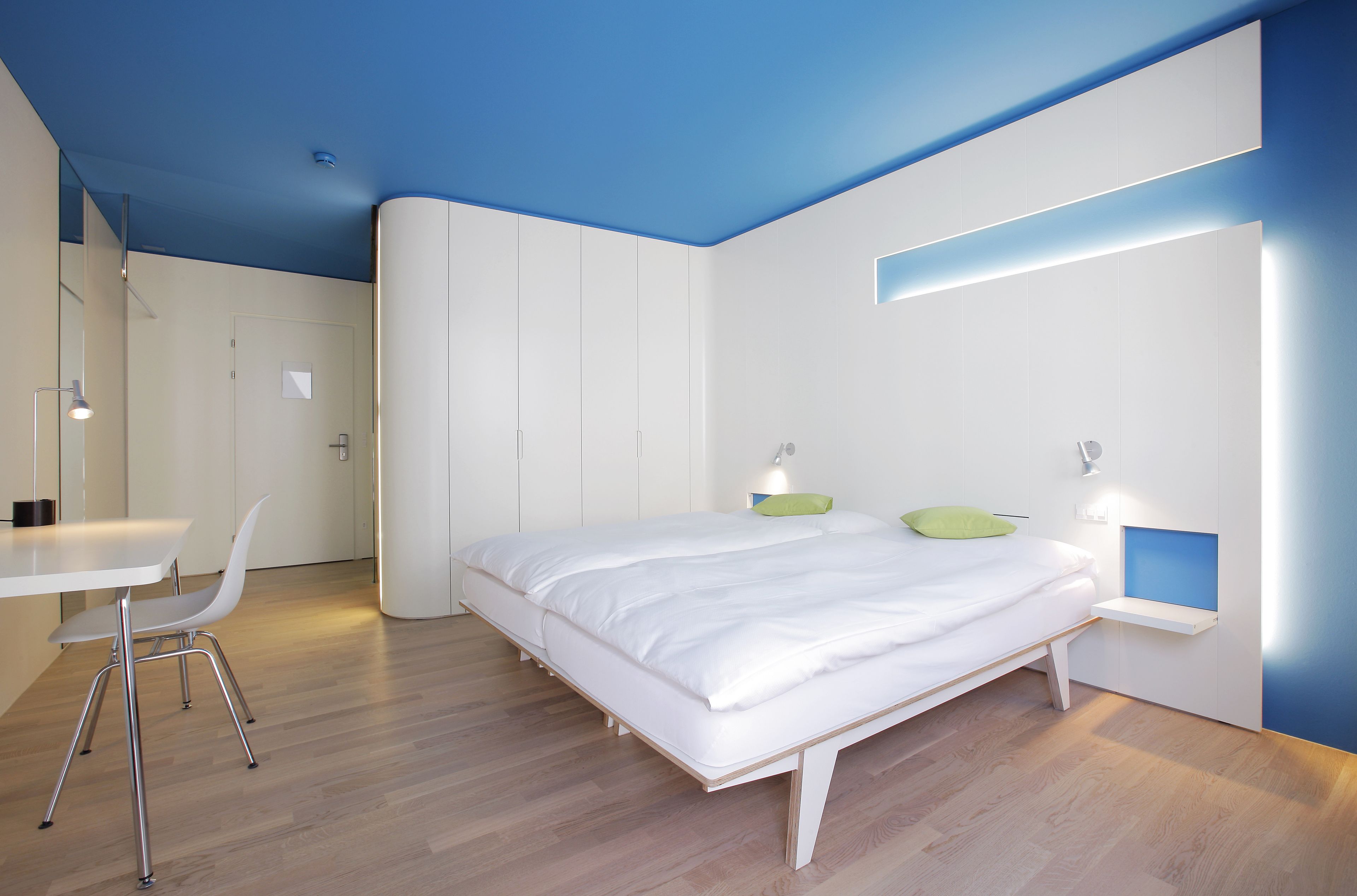 Un dormitorio moderno con cama, mesita de noche y escritorio con silla.