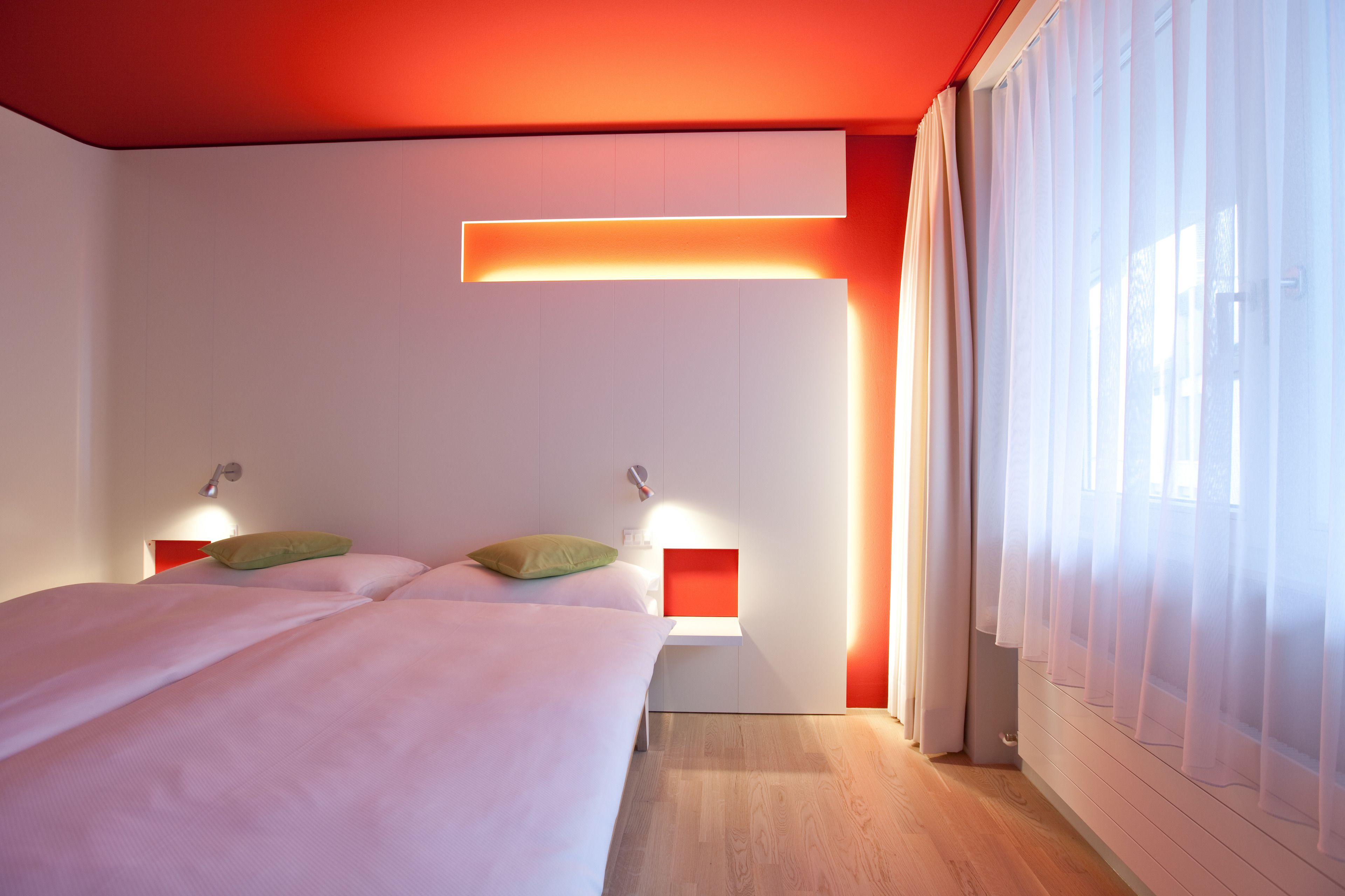 Une chambre d’hôtel moderne avec un grand lit, des tables de chevet et une fenêtre ornée de rideaux légers.