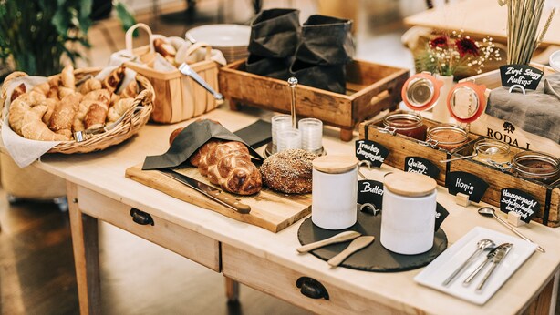 Een houten tafel met diverse etenswaren, zoals brood, gebak en potten met sauzen.