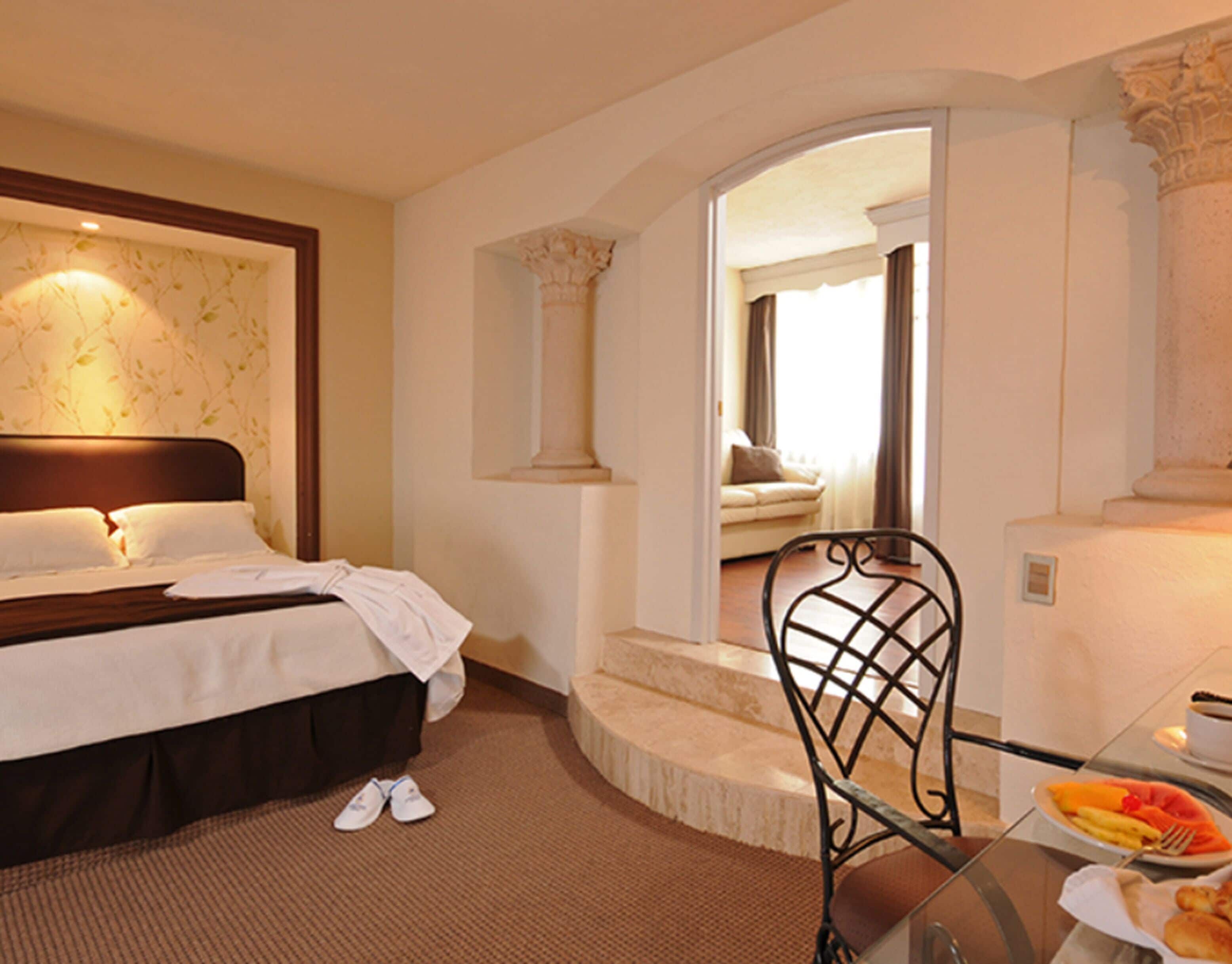 A hotel room with a bed, a chair, a table with breakfast, and a staircase.