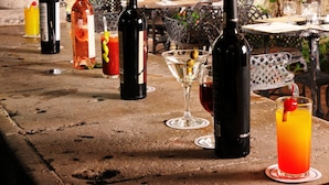 A table set with wine bottles and glasses, surrounded by chairs and a rustic wooden ceiling.