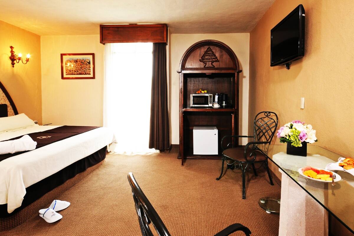 Habitación de hotel con cama, escritorio con desayuno, microondas y televisor.