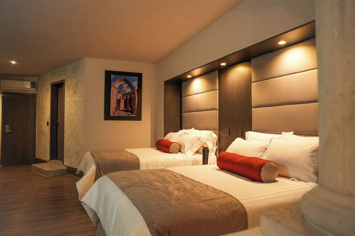 Habitación de hotel con dos camas, un ventanal grande y un cuadro en la pared.