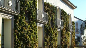 A building with arched windows and balconies, surrounded by a well-maintained garden with various plants and flowers.