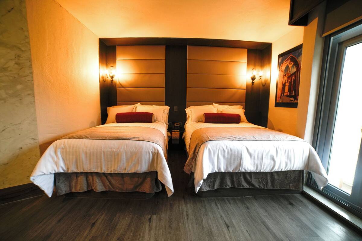 Habitación de hotel con dos camas, piso de madera y un ventanal grande.