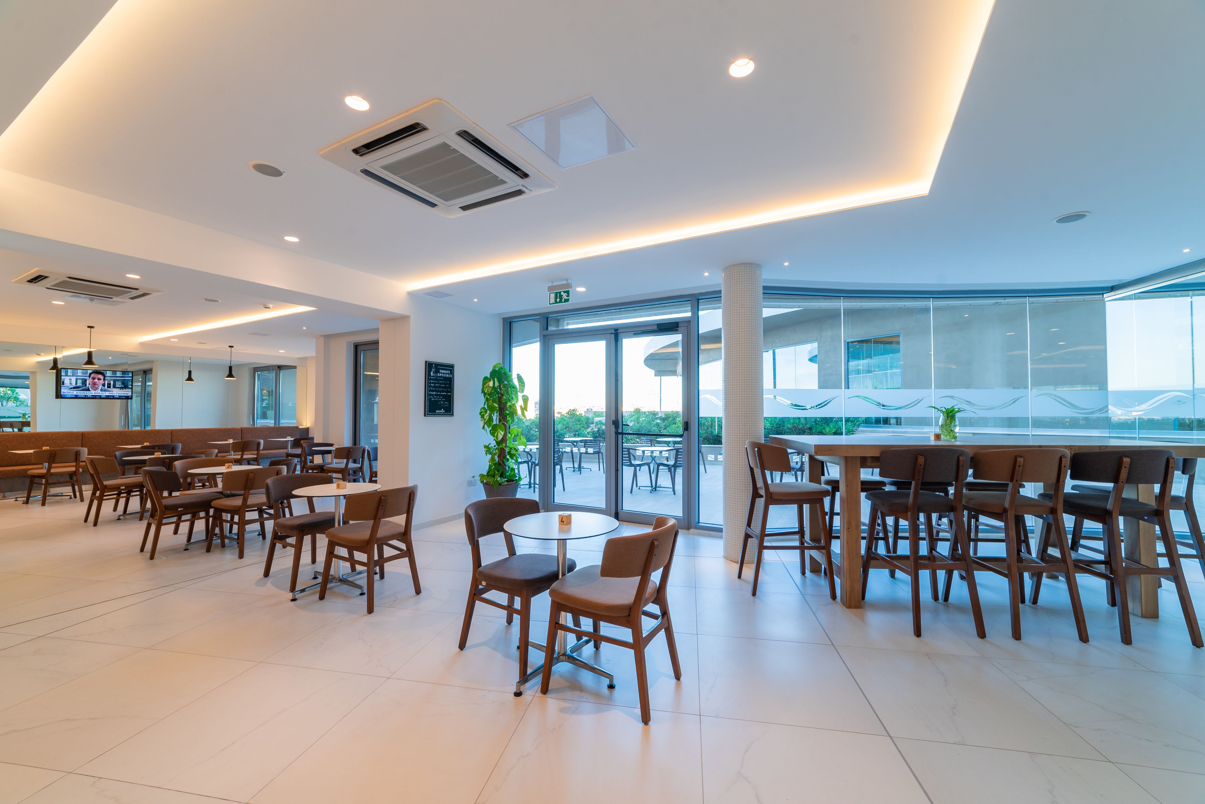Un comedor moderno con mesas y sillas, ventanas amplias y vistas al exterior.