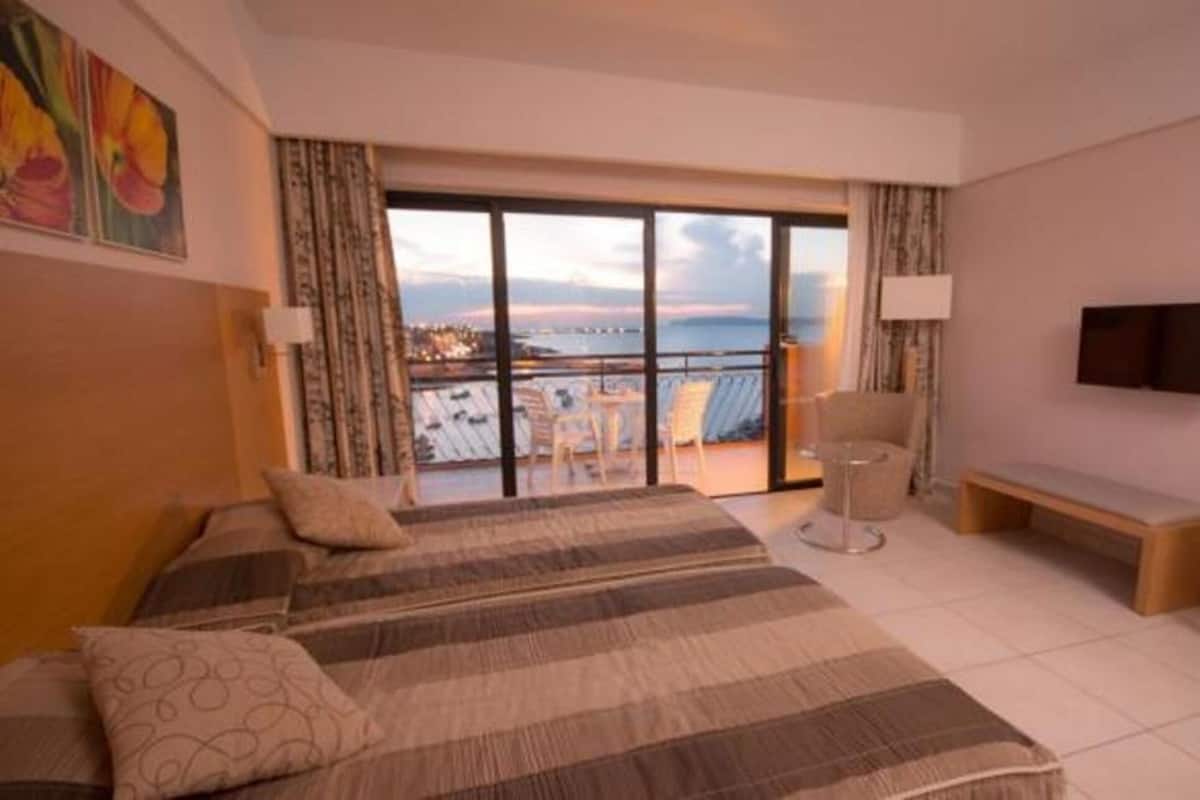 Ein Hotelzimmer mit Bett, Schreibtisch, Stuhl, Fernseher und einem Balkon mit Blick.