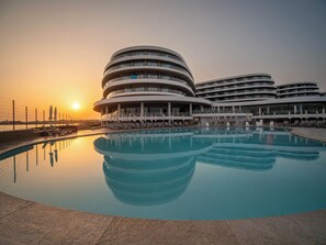 A modern hotel with a circular pool and multiple balconies. - Ramla Bay Resort (Mellieha)