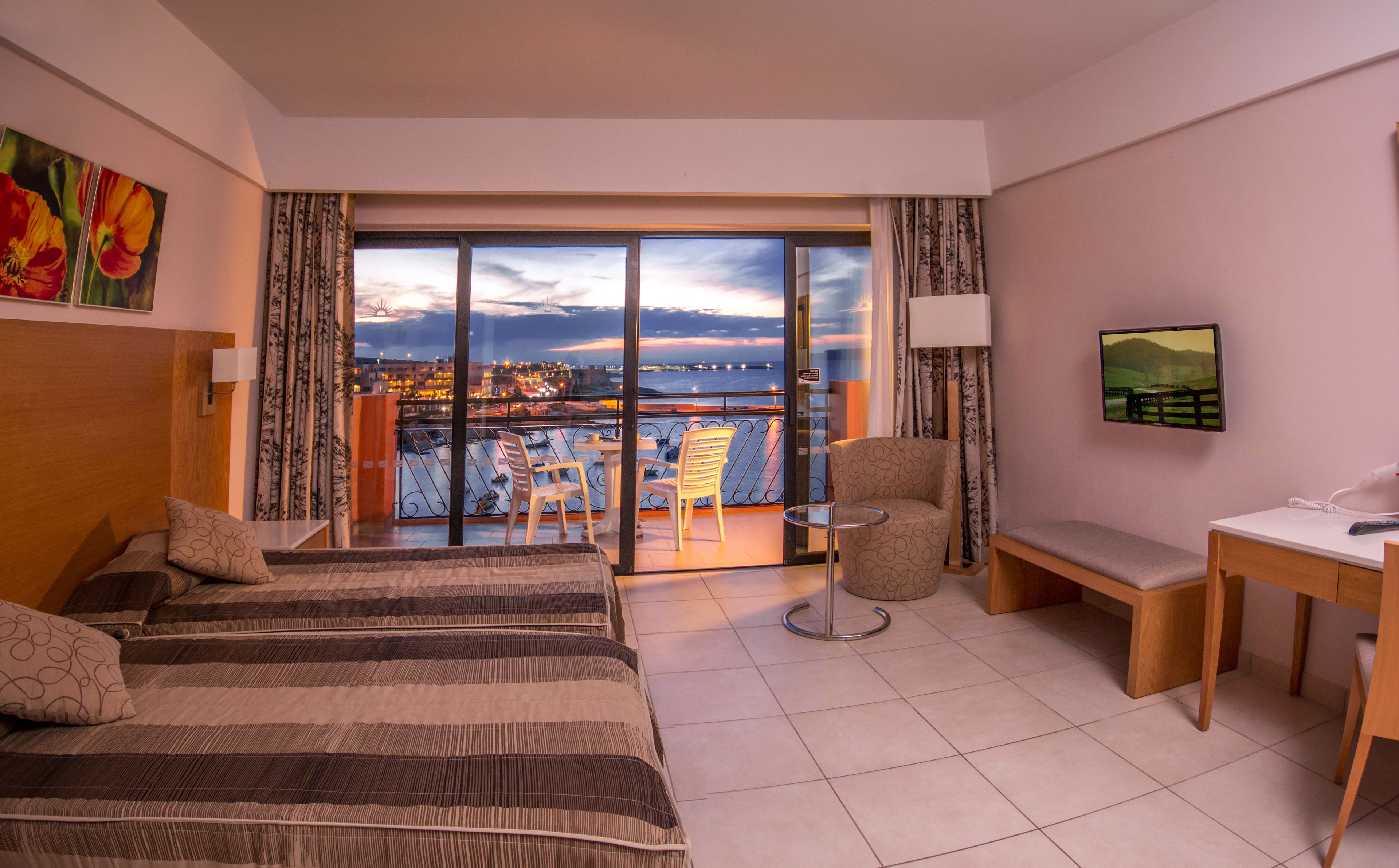 A hotel room with a balcony, a bed, a desk, and a chair.