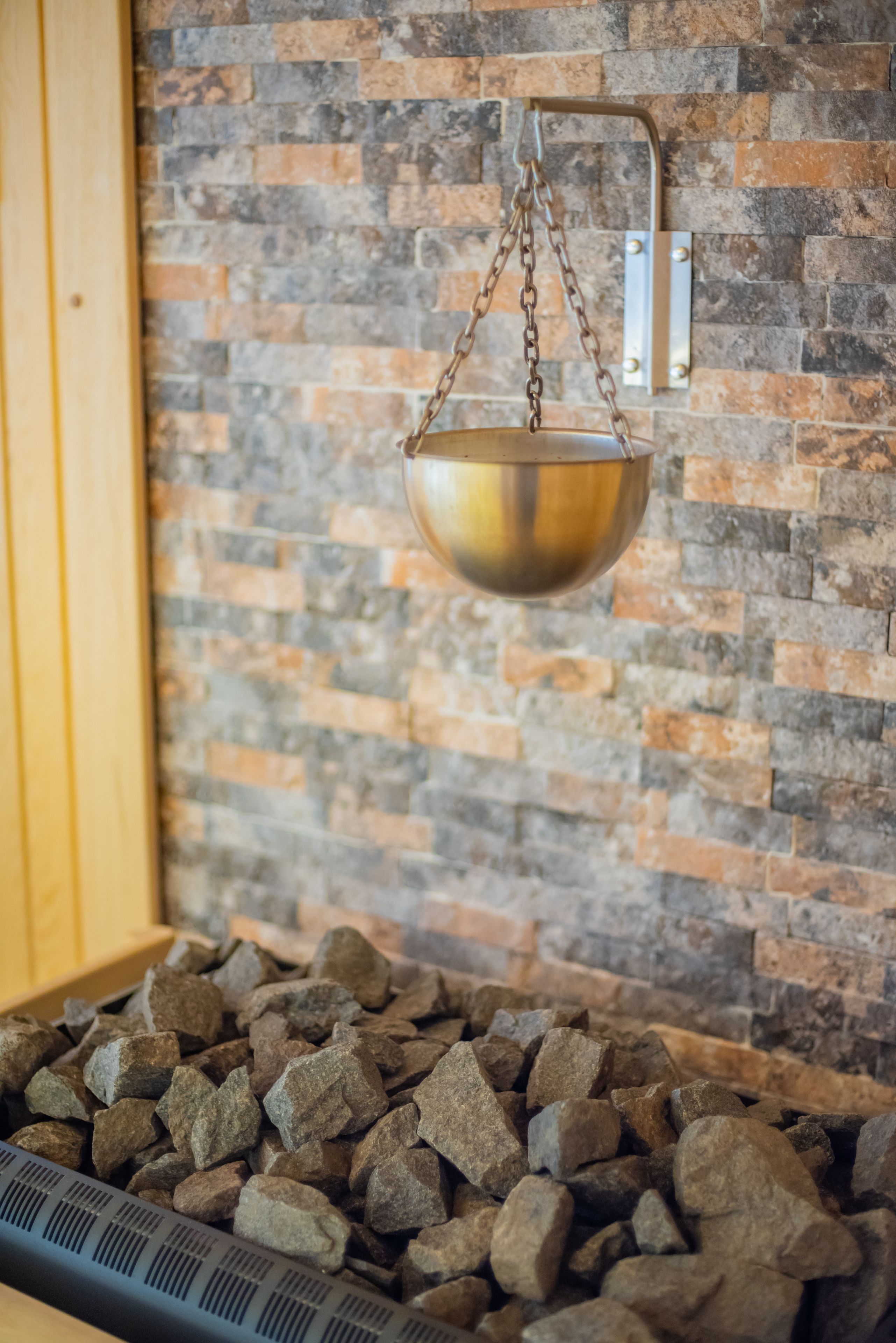 A hanging brass bowl over a bed of rocks, with a brick wall in the background.