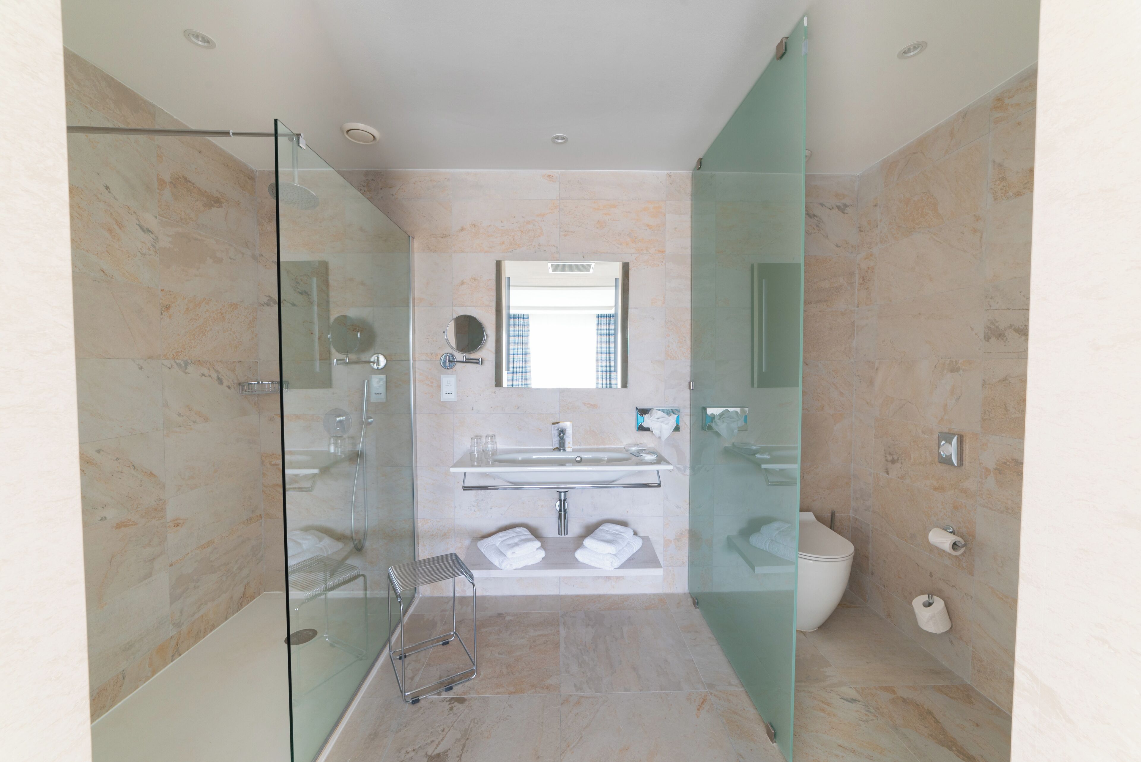 Une salle de bain moderne avec une douche à parois de verre, un lavabo surmonté d’une plaque de verre et des toilettes.