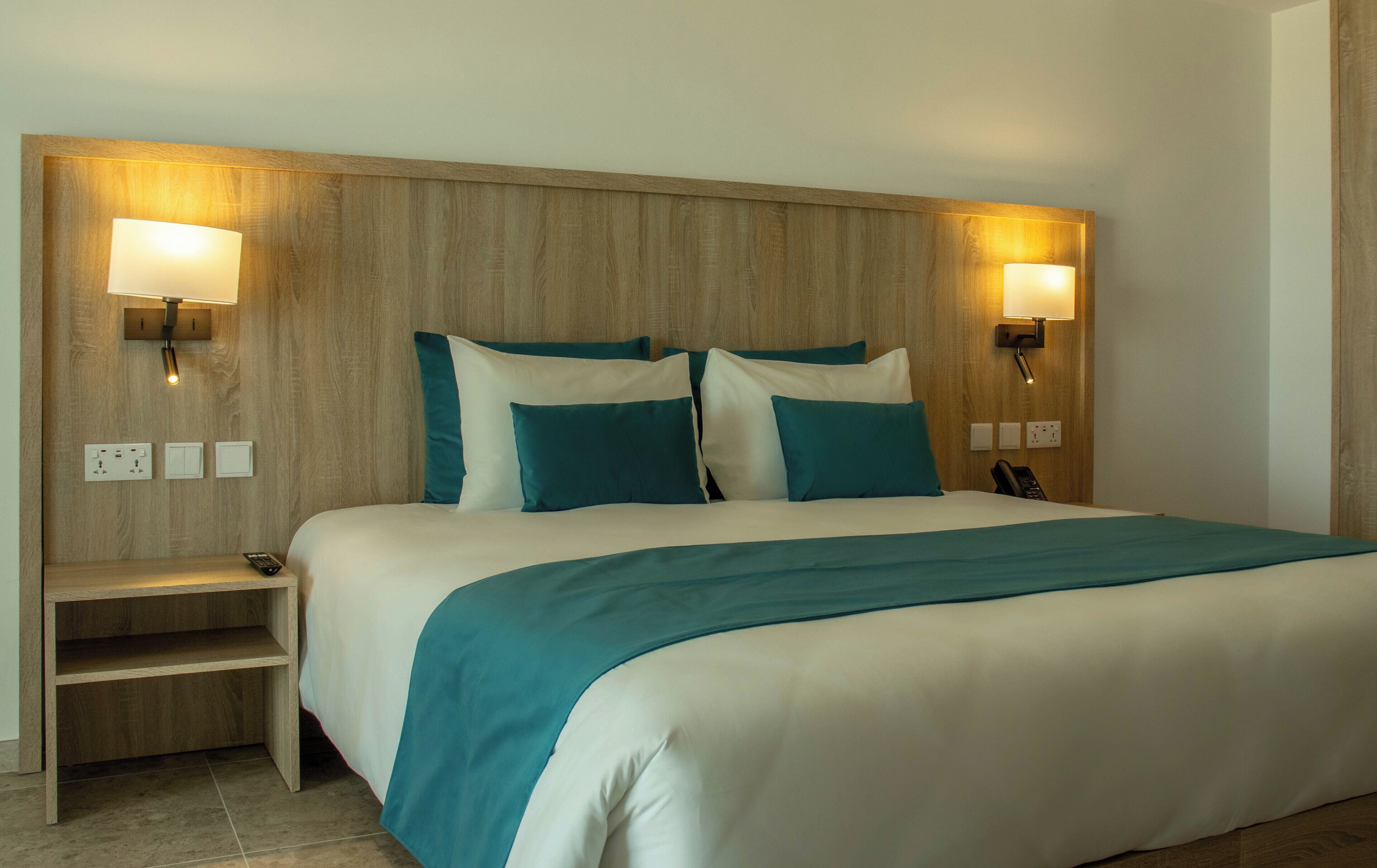 A hotel room with a large bed, two bedside tables, a nightstand, and two wall-mounted lamps.