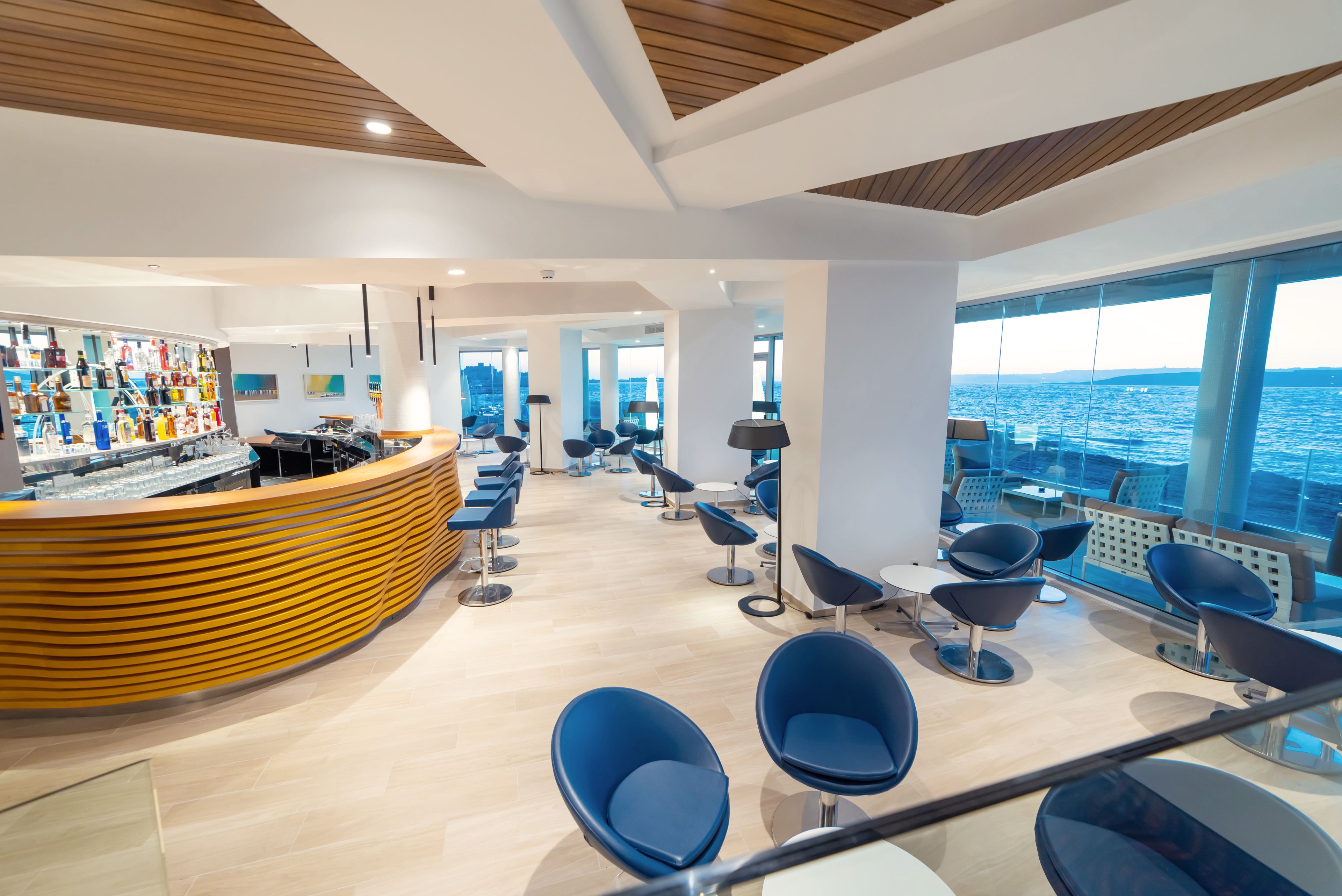 Un interior moderno con un mostrador de recepción curvo, zona de estar y grandes ventanales con vistas al mar.
