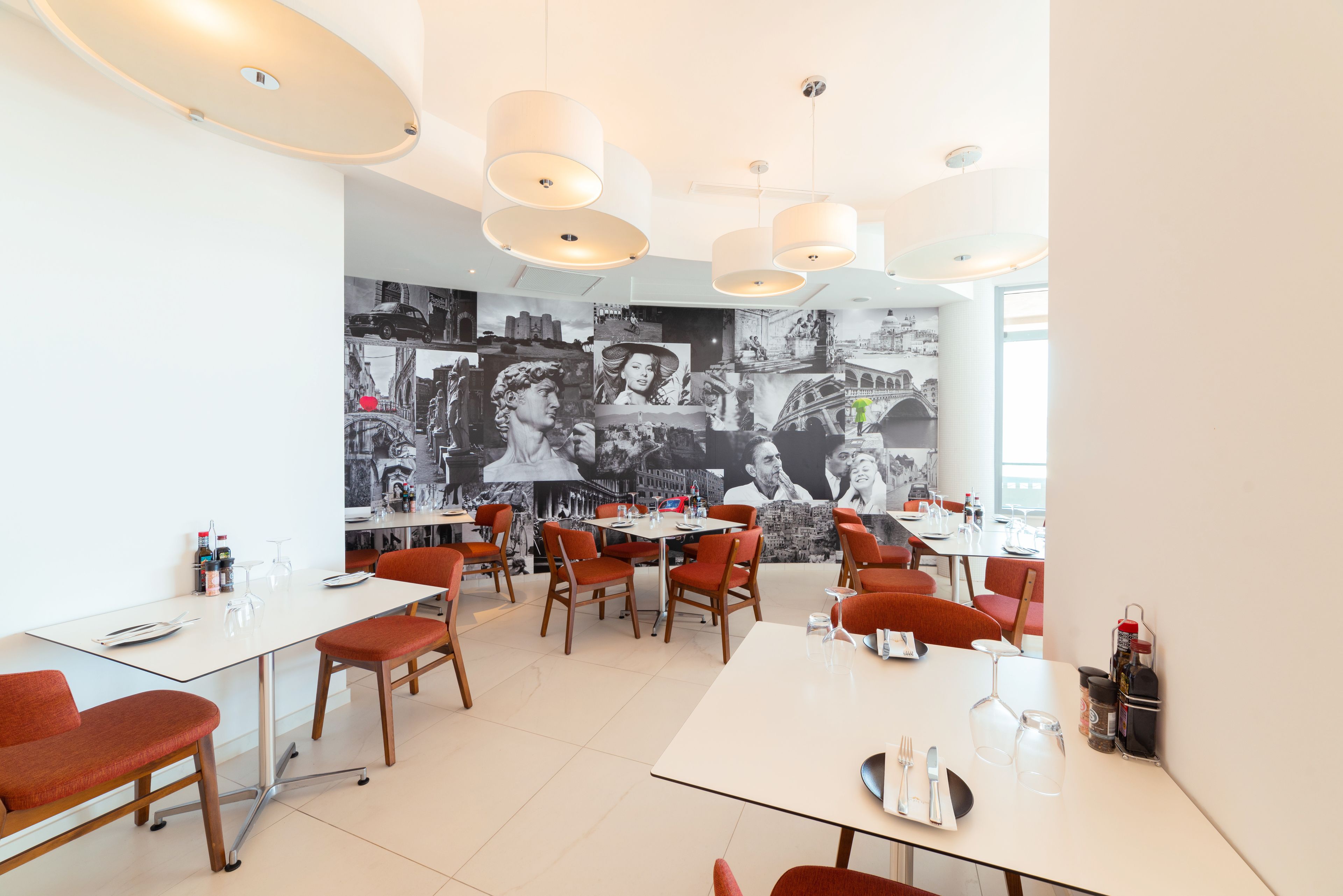 Uma sala de jantar moderna com mesas brancas e cadeiras laranja, com um grande mural na parede do fundo.