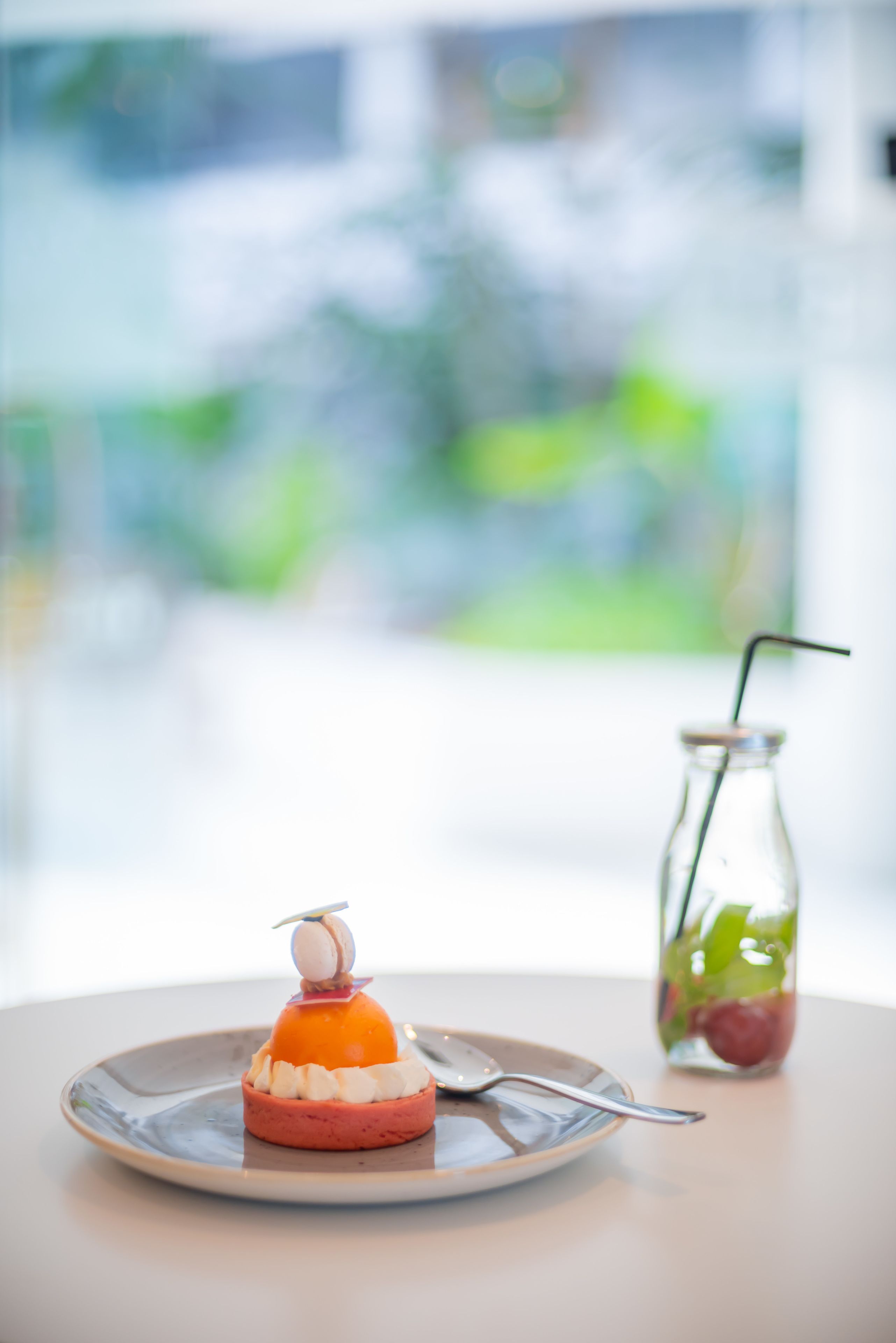 A dessert on a plate with a spoon and a glass of drink with a straw.