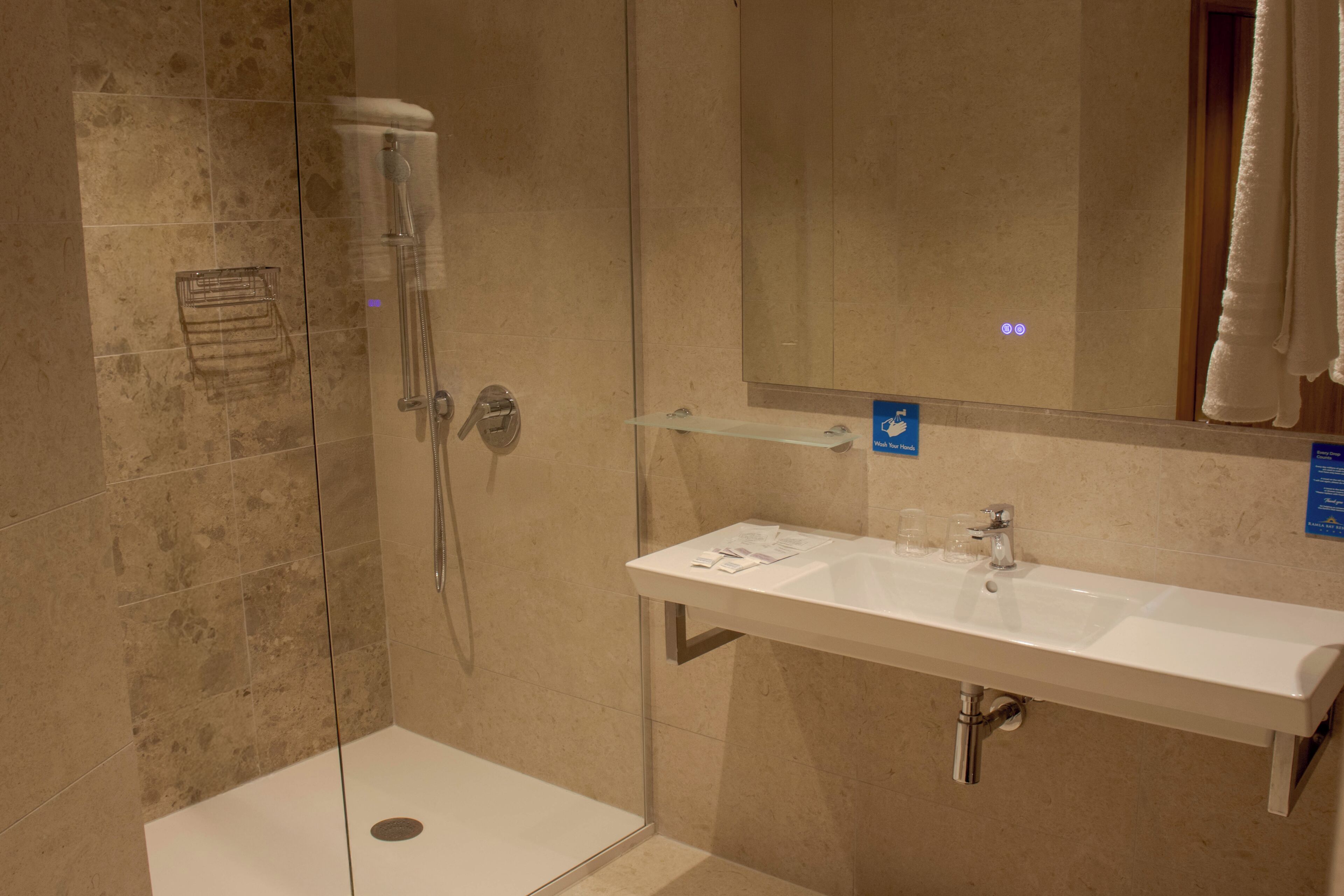 Un bany modern amb dutxa de vidre, un lavabo blanc amb un mirall a sobre i un suport per a tovalloles.