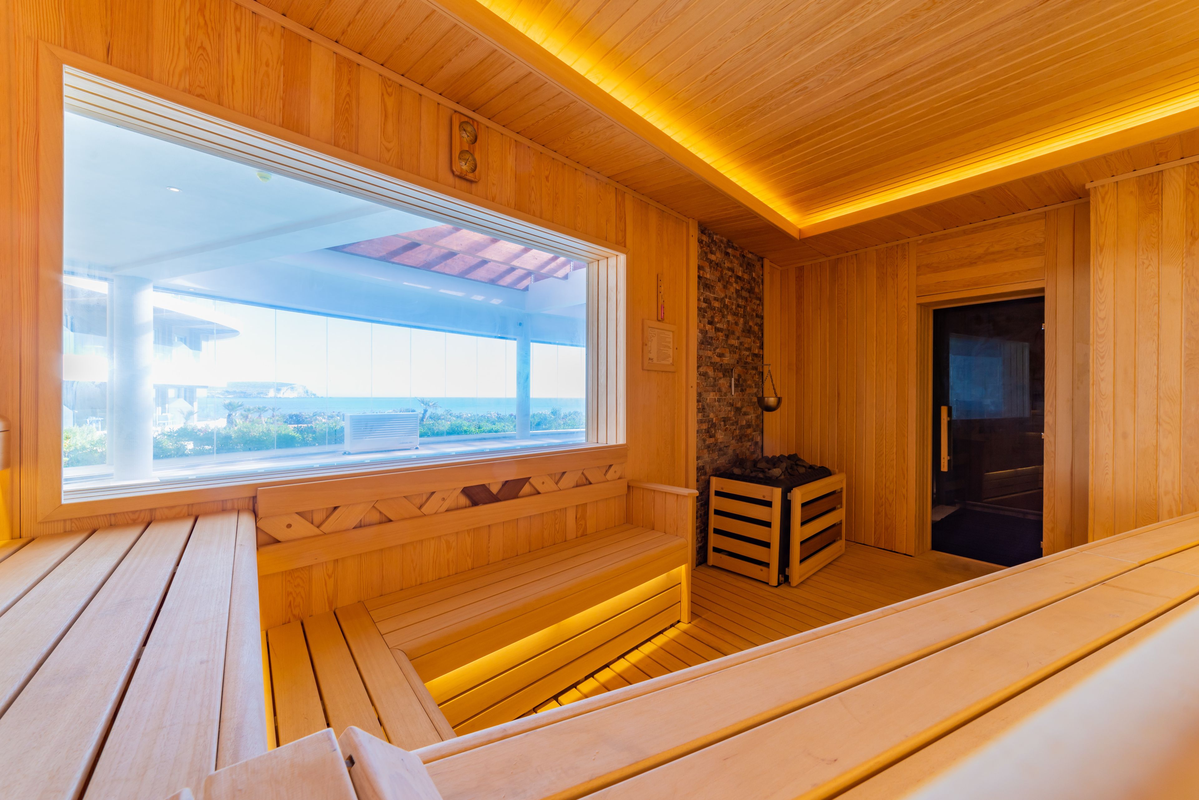 Una sauna de madera con bancos, pared de piedra y ventana con vistas.